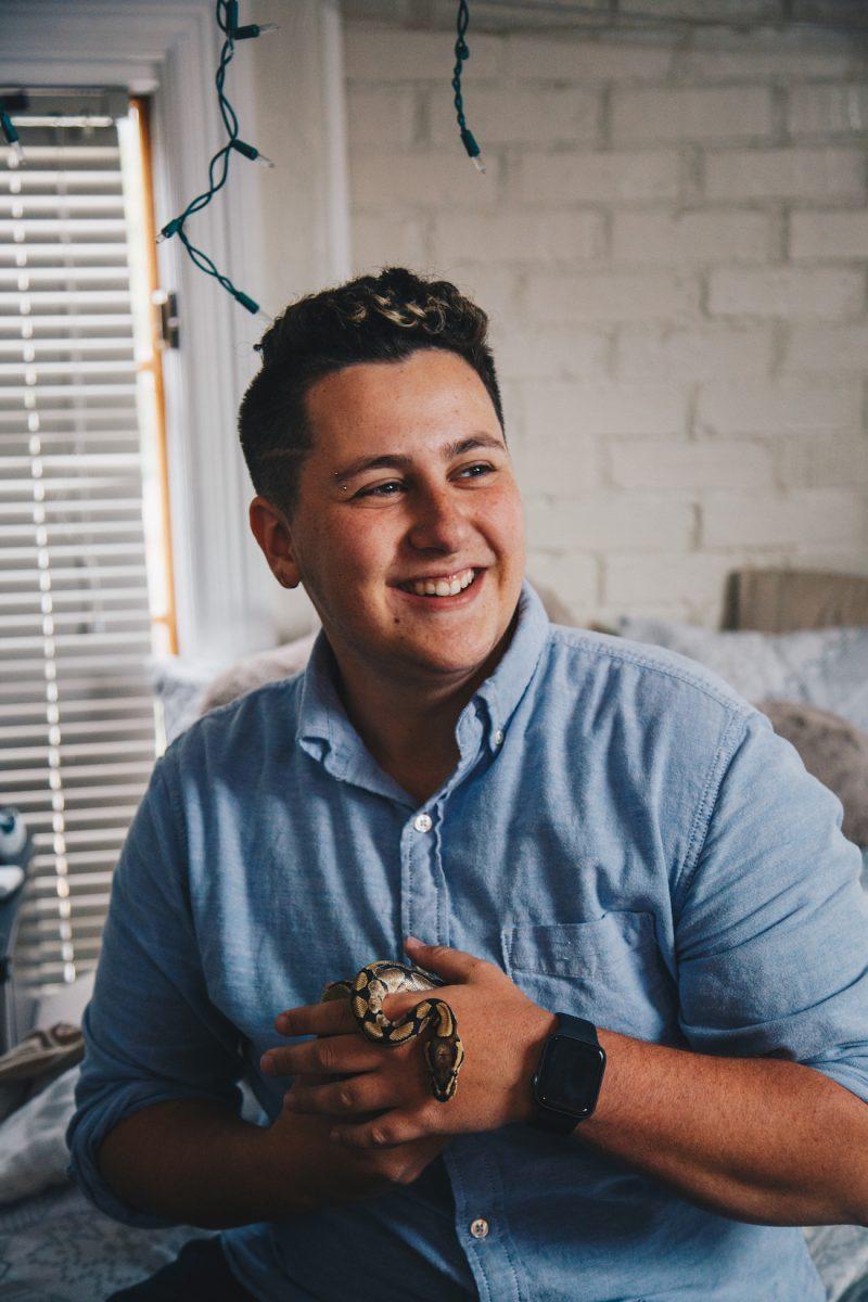 On a rainy Saturday, Oliver Cochener sits on his bed in the large attic room of the DU house and plays with his fire ball python Gerald. (Sarah Northrop/Emerald)