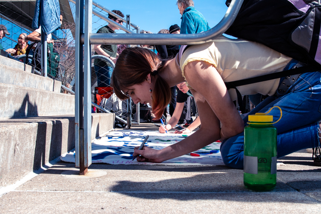 A student attendee signs a "School Strike 4 Climate Climate" flag. Eugene youth lead a climate strike march on March 15, 2019, ending in a protest at the Federal Courthouse. (Maddie Knight/Emerald)