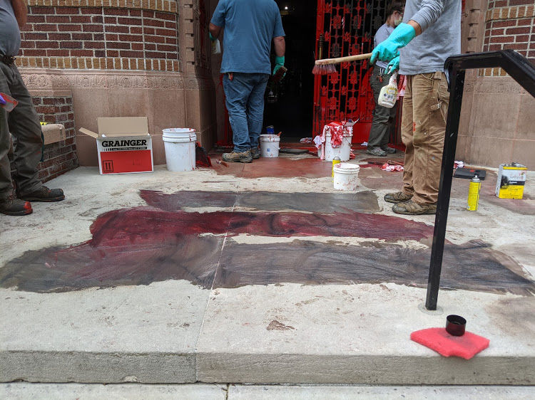 Facilities management staff clean up vandalism outside of the Knight Library, including the spray-painted words "whose racist heritage" and "Schill hated Charlie" (Sally Segar/Daily Emerald)