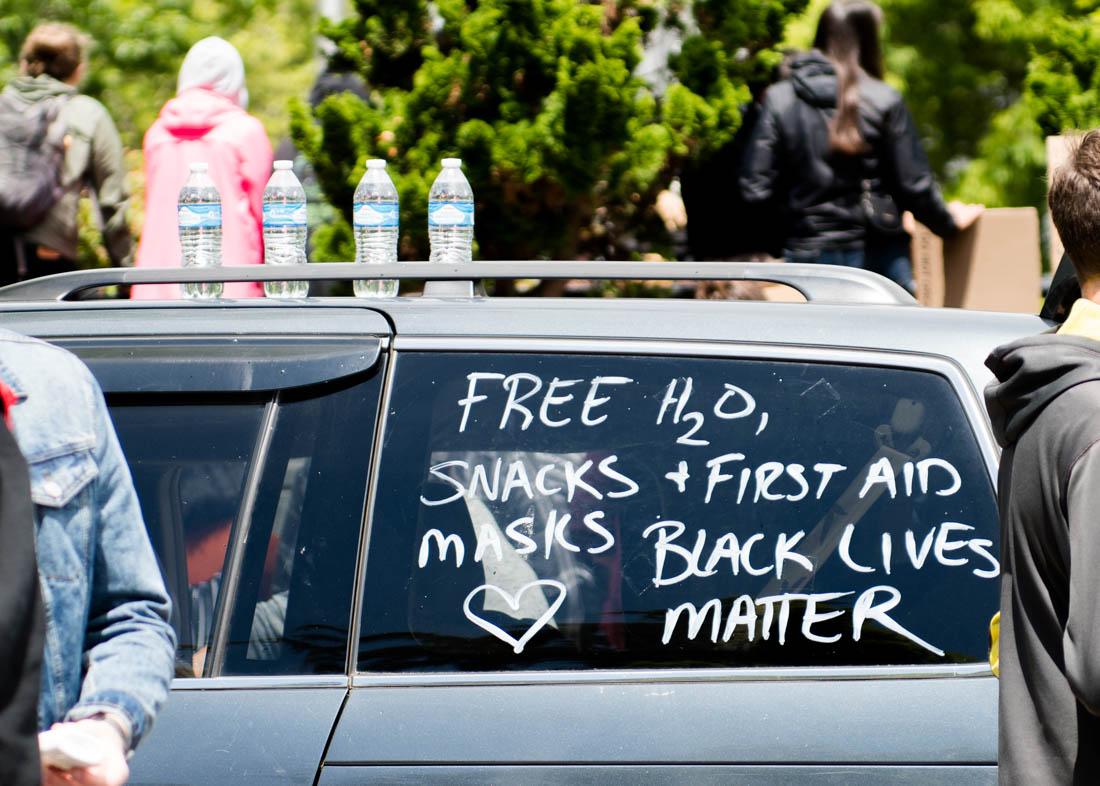 A small group that identifies themselves as white allies hands out water, first aid supplies, and masks at the protest. The car continues to drive around while protestors march through the city of Eugene. The BIPOC Liberation Collective leads a protest in downtown Eugene, Ore. on June 7th, 2020. (Madi Mather/Emerald)