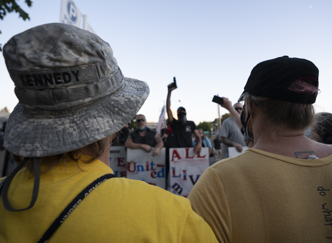 A Wall of Moms protester held arms in front of counter-protesters while one All Lives Matter protester raised his firearm. All Lives Matter protested against anti-racists outside the Federal Courthouse on Saturday, July 25, 2020, at 8 p.m. in Eugene, Oregon. The confrontation turned violent after physical altercations. The standoff ended two hours later when anti-racists marched the All Lives Matter group away. (Kevin Wang/Daily Emerald)