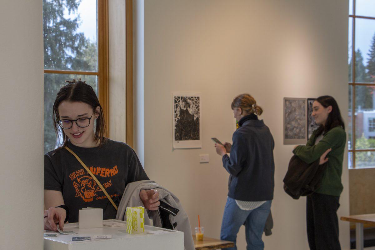 Artist Gracie Cummings (junior) looks through letterpress cards by Mia Radostitz (junior). Students and supporters gather for the &#8220;Im-pressed&#8221; art reception in the EMU Adell McMillan Gallery on April 21st, 2022. (PaigeRodriguez/Emerald)