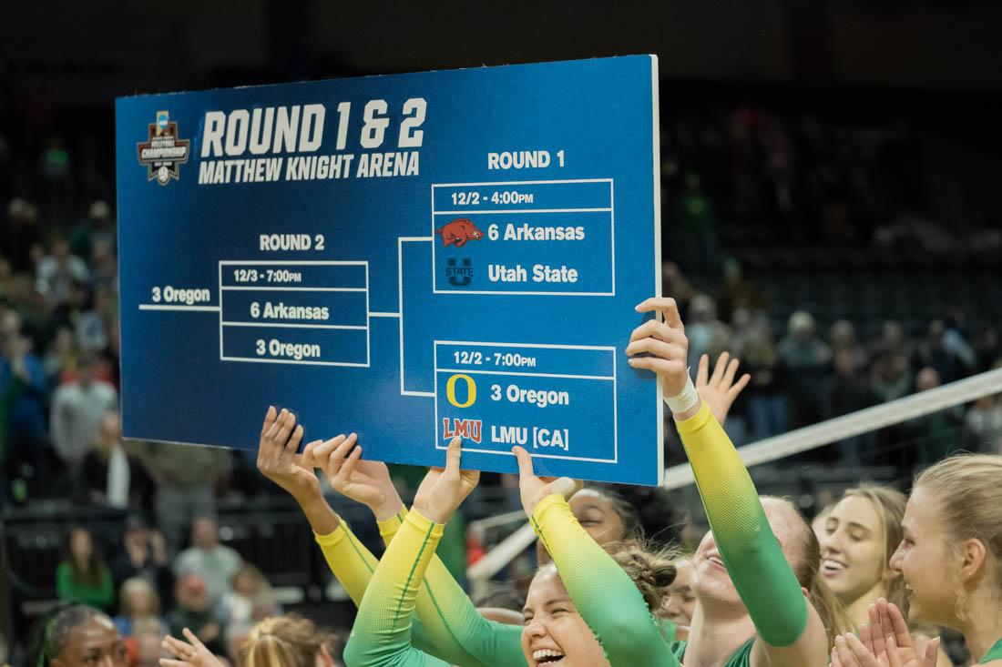 The team celebrates at center court after adding Oregon to the next round of the tournament poster. Oregon Women&#8217;s Volleyball host their second round NCAA Volleyball Championship Tournament opponent the Arkansas Razorbacks at Matthew Knight Arena in Eugene, Ore., on Dec. 1, 2022. (Skyler Davis/ Emerald)