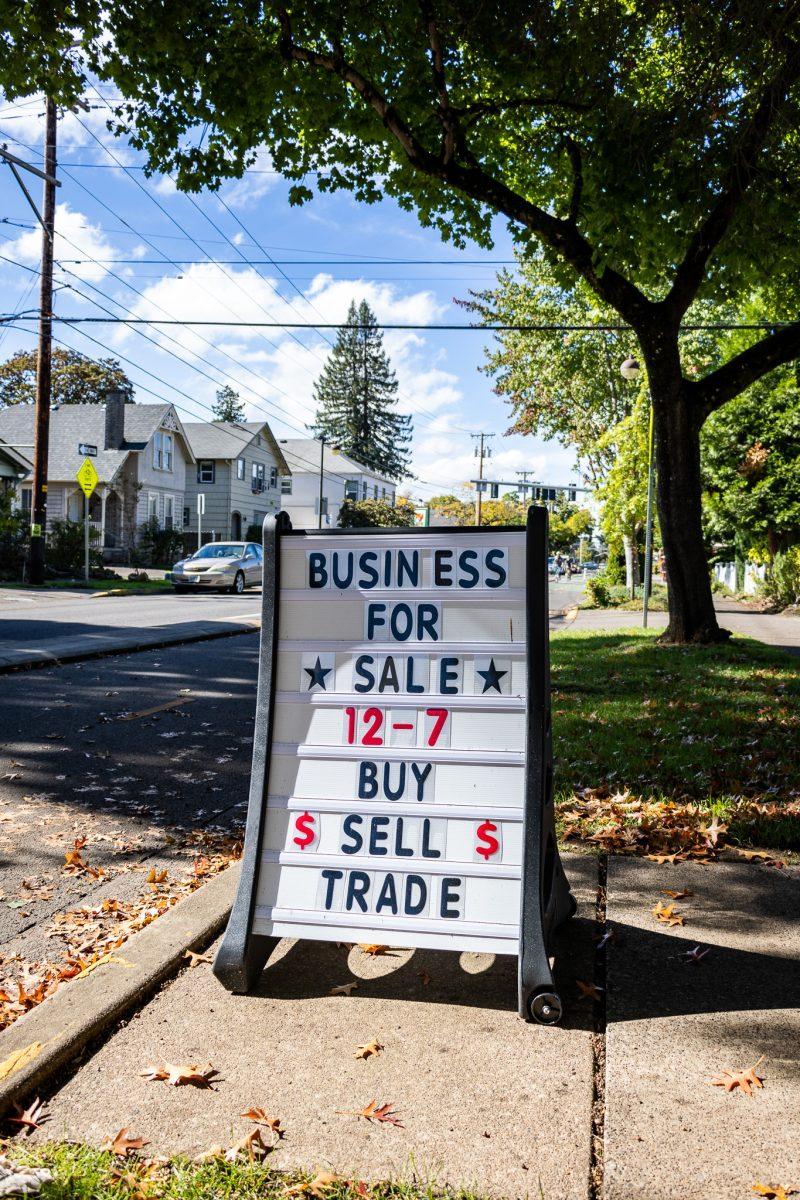 A sign stands on a bustling 13th street welcoming all people going about their day to enter the store. (Jonathan Suni/Emerald)