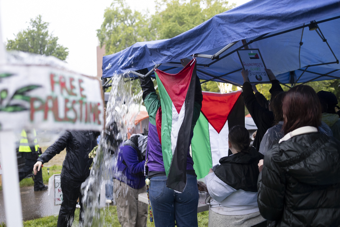 Demonstrators dump water that had gathered on top of a canopy inside of the encampment on May 3, 2024. This is the fifth day of the growing pro-Palestine encampment demonstration, which now fills most of space between Lillis Business Complex and Knight Library; the protest is one of many across college campuses nationwide. (Alex Hernandez/Emerald)