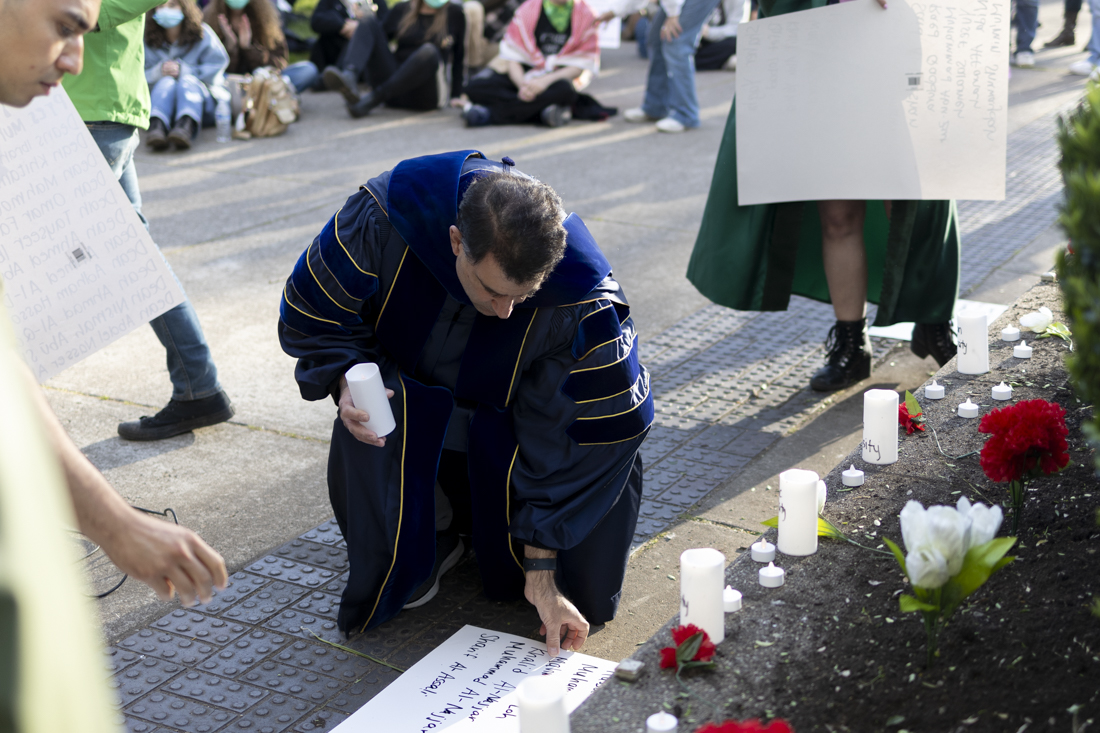 A UO faculty member picks up a sign and candle to deliver to Johnson Hall after the vigil on May 7, 2024. Protesters gathered in front of the encampment demonstration on the UO Memorial Quad for a "Scholasticide Vigil" and speak-out, where UO faculty members spoke in support of Palestine and student protesters before delivering a signs and candles&#8212;referring to destroyed universities and academics who have been killed in Gaza&#8212;to Johnson Hall. (Alex Hernandez/Emerald)