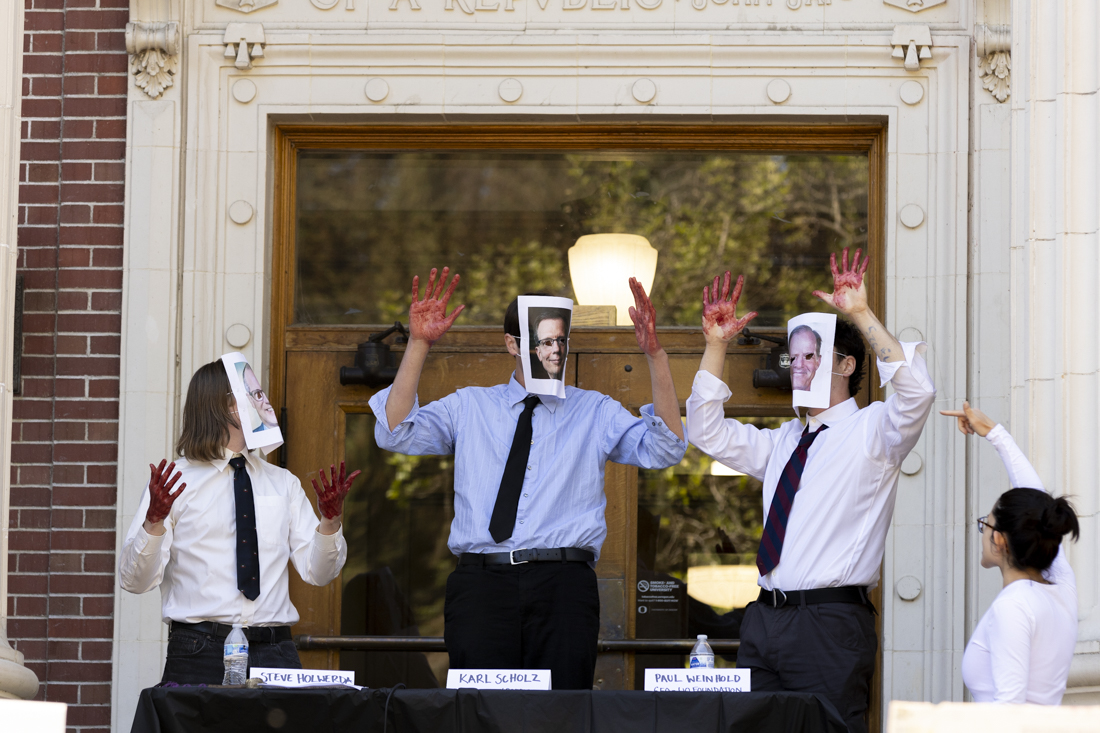 Protesters yell and chant as the "defendants" in the mock trial demonstration raise their hands, covered in red, on May 16, 2024. Protesters marched to Johnson Hall to hold a "mock tribunal," charging UO President John Karl Scholz, UO Foundation President Paul Weinhold and UO Board of Trustees chairperson Steve Holwerda with "complicity in genocide," according to Salem Younes, a leader of the UO Coalition for Palestine; the crowd found the trio "guilty," and the tribunal was followed by a sit-in on the steps of the building. (Alex Hernandez/Emerald)