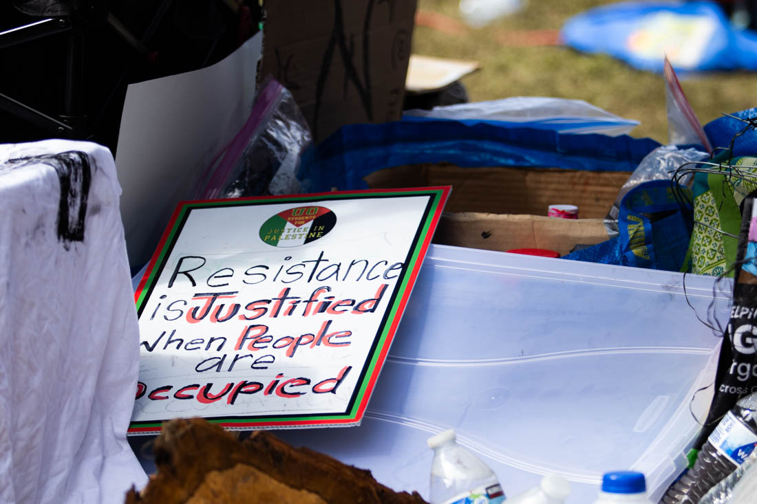 A glimpse into the encampment through one of their signs, stating "Resistance is Justified When People are Occupied". Hundreds of protesters gathered at the site of the encampment on campus, the Memorial Quad, and protested in support of Palestine on May 7, 2024. (Mason Cruz/Emerald)