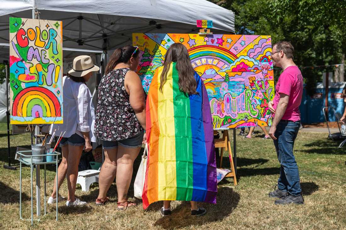 Several attendees and a volunteer look at the community painting at Cassie Genc&#8217;s art booth. The Eugene Pride Festival took place at Alton Baker Park in Eugene, Ore. on Saturday, Aug. 12th, 2023. (Molly McPherson/Emerald)