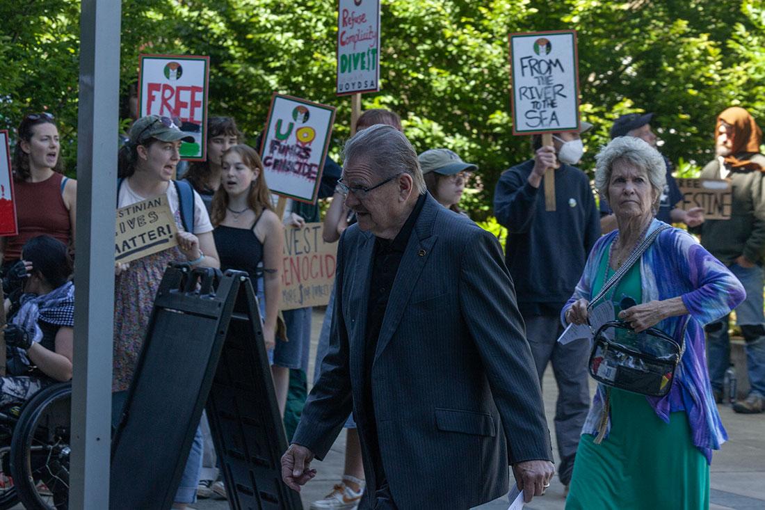 Attendees walk past the gathered crowd of protestors. Thursday, President of the University of Oregon, Karl Scholtz, attended his investiture at the Matthew Knight Arena, celebrating his formal installment as president of the university. Pro-Palestine protestors interrupted the ceremony as Scholtz accepted the Centennial Medallion with a deluge of chants. After a brief confrontation, protestors moved outside to a separate entrance where they continued their protest. (Miles Cull/Emerald)