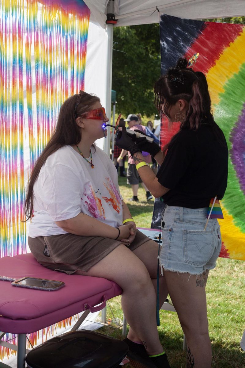 An artist at Memento Ink fixes a tooth gem to an attendee.(Miles Cull/Emerald)