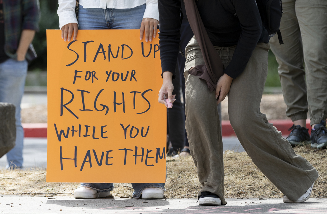 A demonstrator stands after writing a message in chalk on the sidewalk at the protest outside of Oregon Hall—which was organized against the university's punitive measures toward students involved in previous protests—on August 15, 2024. (Alex Hernandez/Emerald)