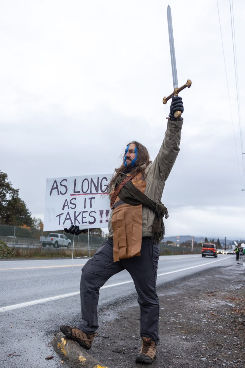 A striking employee holds a sign that reads "AS LONG AS IT TAKES!" On Oct. 31, 2024 Bigfoot Beverage employees continue their strike in Eugene, Ore. Teamsters Locals 206 and 324 have been on strike against Bigfoot Beverages since Sept. 19, 2024. Bigfoot Beverages tried to replace the Teamsters’ pensions with a 401(k) plan sparking the strike from the two Locals. (Molly McPherson/Emerald)