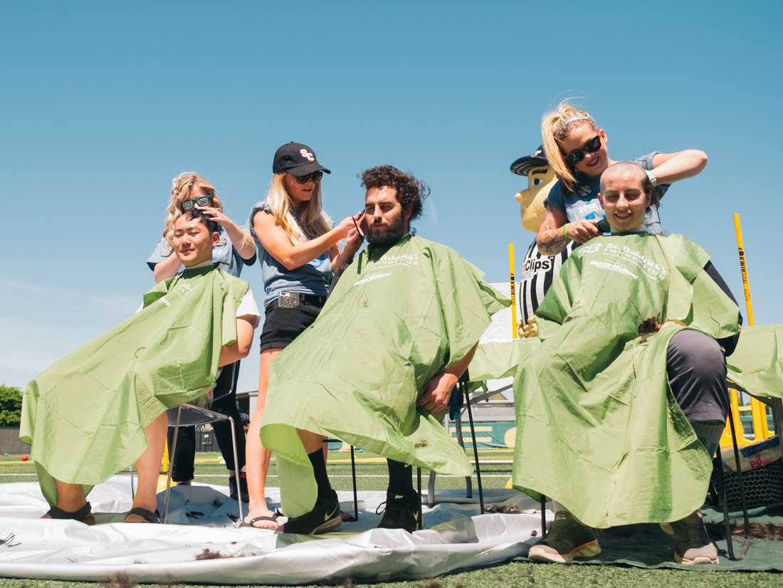 Three volunteers sit as they get their heads shaved in front of the crowd. St. Baldricks Foundation hosts a fundraising event to raise awareness for child cancer research at the Pap&#233; Field in Eugene, Ore. on May 11th, 2019. (Connor Cox/Emerald)