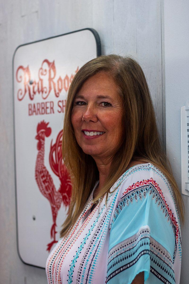 Karyn Shields poses next to a sign advertising the Red Rooster barber shop on 13th Avenue in Eugene, Oregon. Karyn Shields is the owner of the Red Rooster barber shop, which was opened by her father in 1968.