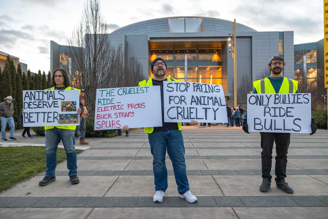 <p>Three protesters stand in front of the east entrance of Matthew Knight Arena. Protesters gather outside Matthew Knight Arena to protest the Profesional Bull Riders event taking place inside the arena, on Feb. 18th, 2023. (Molly McPherson/Emerald)</p>