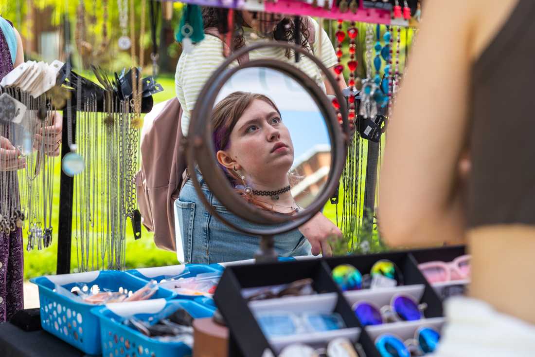 A patron looks at jewelry hanging on the frame of the tent. The ASUO Street Faire happens twice a year, once during the fall term and once during the spring term. This year, the Street Faire is open from 10 a.m. to 6 p.m. on May 10 through May 12. (Molly McPherson/Emerald)