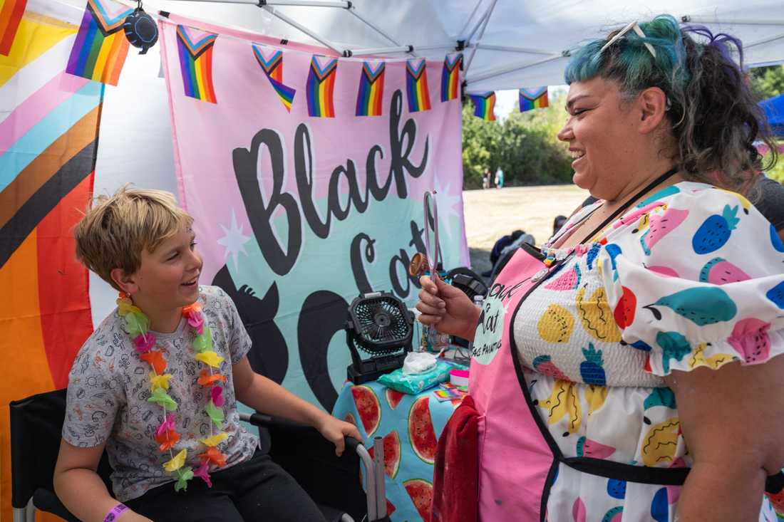 A child, who just got his face painted at Black Cat Face Painting, smiles as he looks at his face paint in the mirror for the first time. The Eugene Pride Festival took place at Alton Baker Park in Eugene, Ore. on Saturday, Aug. 12th, 2023. (Molly McPherson/Emerald)