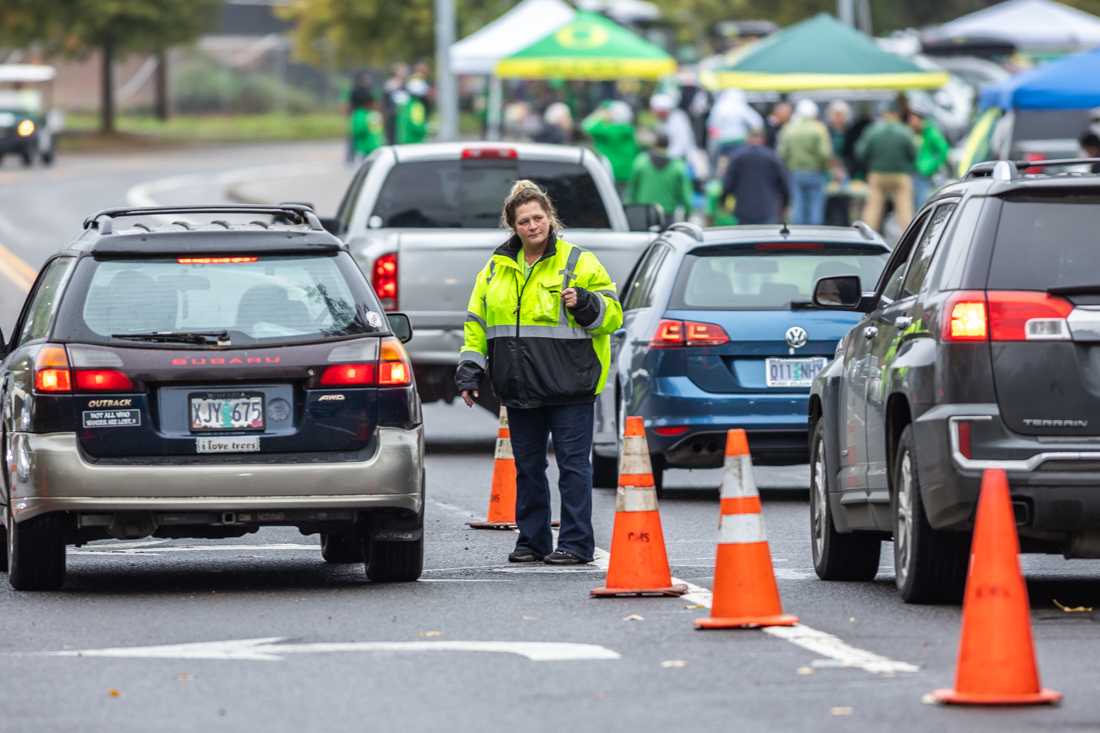 A parking attendant directs oncoming cars toward the proper parking lot based on their parking pass. Hundreds of workers flock to and around Autzen Stadium on gamedays, their work is often overlooked by the thousands of fans who attend the game. (Molly McPherson/Emerald)