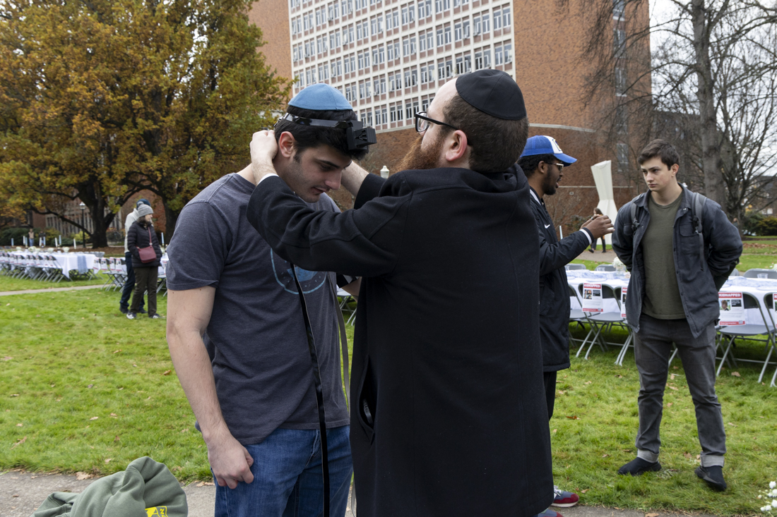 Chabad Rabbi Berel Gurevitch helps one of the demonstration's attendees put on Tefillin, a set of leather straps and boxes with Hebrew scrolls inscribed with verses of the Torah inside. (Alex Hernandez/Emerald)