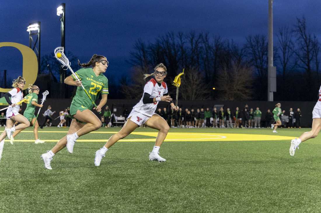 Oregon midfield Lexi Jenkins (23) caries the ball down the field against Youngstown State defender Jocelyn Fike (16). The Oregon Women's Lacrosse team won their match 19-8 against Youngstown State University at Pape Field on Feb. 9, 2024. (Alex Hernandez/Emerald)