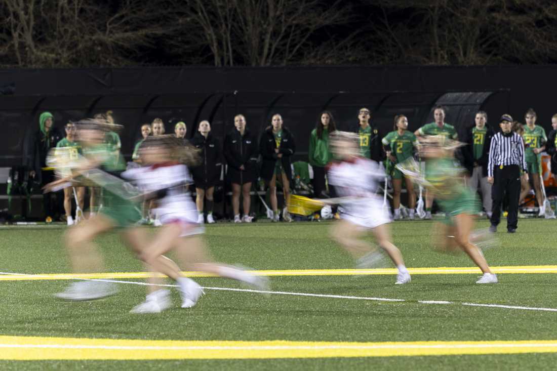 Players run down the field as the team watches from the sidelines. The Oregon Women's Lacrosse team won their match 19-8 against Youngstown State University at Pape Field on Feb. 9, 2024. (Alex Hernandez/Emerald)