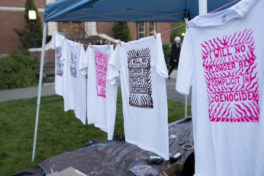 Shirts with pro-Palestine messages hang from tents as people line up to receive shirts, patches and other items inside of the encampment on April 30, 2024. Students and community members are on their second day of a pro-Palestine encampment demonstration on the UO Memorial Quad; the protest is one of many across college campuses nationwide. (Alex Hernandez/Emerald)