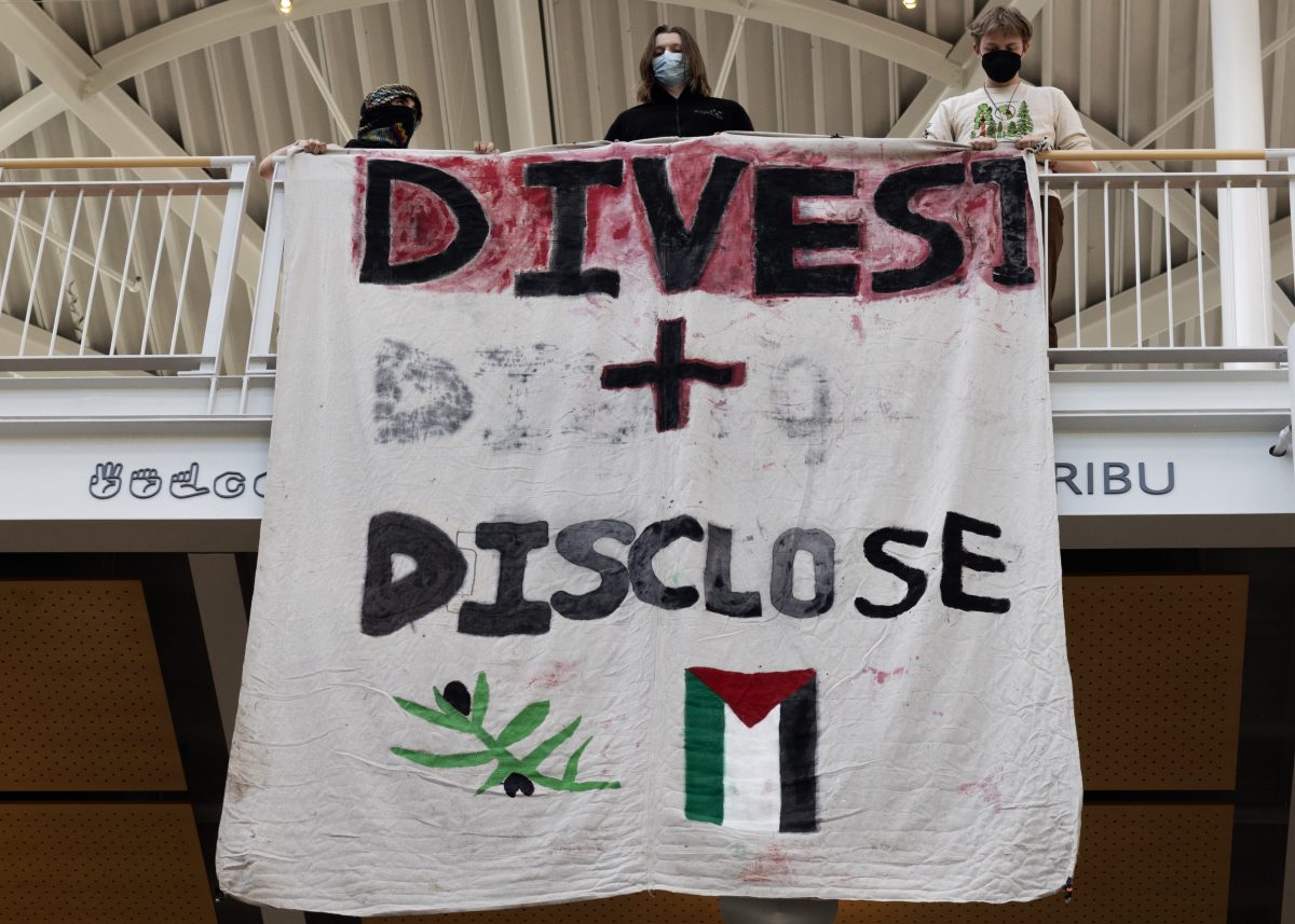 Protesters drape a banner that reads, "Divest + Disclose" on the second floor of the Lillis Business Complex. Protesters gathered on May 20, 2024, for a "100 Hours in Chains" rally in front of Johnson Hall&#8212;now "renamed" by protesters to "Alareer Hall," after writer and poet Refaat Alareer, who was killed in Gaza&#8212;with students who had chained themselves to the building removing their chains before marching through other buildings on campus; the rally is the most recent in a series of pro-Palestine demonstrations on the UO campus. (Colleen Bogdan/Emerald)