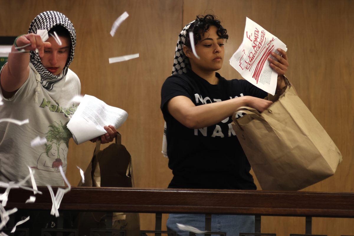 Two protesters toss scraps of paper with phrases like "We charge UO w/ genocide!" and copies of UO's response to their demands around Johnson Hall. On May 10, 2024, hundreds of protesters marched through campus after UO officials did not appear for negotiations. (Colleen Bogdan/Emerald)