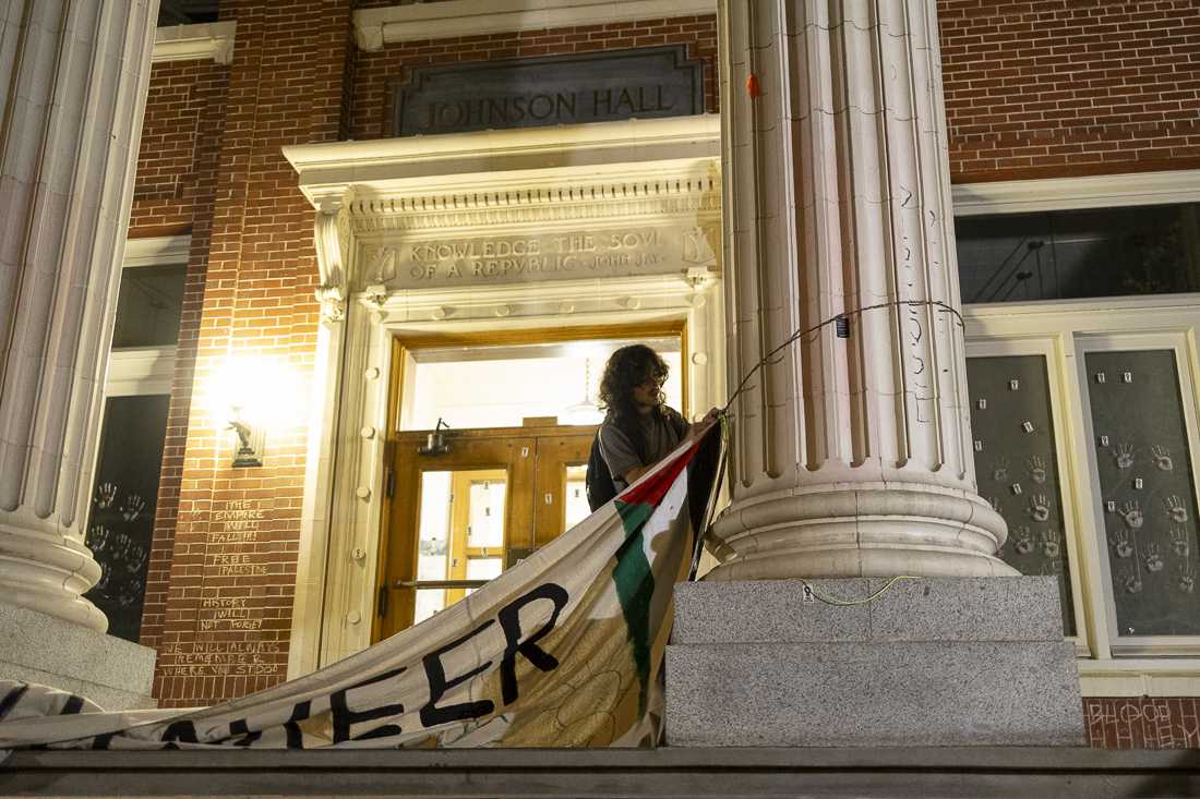 A demonstrator works on taking down the banner reading "Alareer Hall"&#8212;the name demonstrators gave to Johnson Hall, in honor of a Palestinian poet and writer Refaat Alareer&#8212;on May 22, 2024. After weeks of protest, the 24-day-long encampment demonstration saw its end after negotiations teams from the encampment and the University of Oregon reached an agreement to end the encampment in exchange for meeting some student demands, including "No adverse action" for "protected speech" activities, a call for a ceasefire in Gaza, and more. (Alex Hernandez/Emerald)