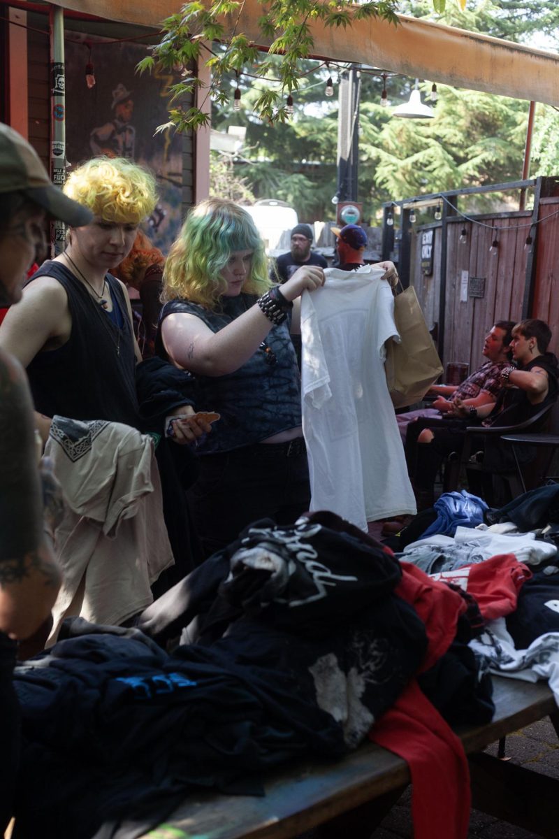 Attendees gather at the punk clothing swap at Sam’s Bonds Garage. The clothing swap encouraged people to bring their clothes to swap out with what they wanted from the tables. Alongside the swap, live music was present inside the bar. (Miles Cull/Emerald)