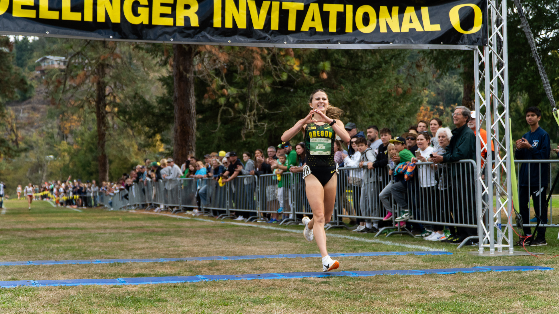 Maddy Elmore throwing up an O with her hands as she cruises across the finish line, winning the womens race of the Dellinger Invite with a gap of 9.6 seconds. (Saj Sundaram/Emerald)