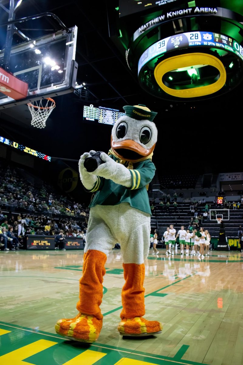 The Oregon Duck holds up a camera as if to take a picture of the photographers seated on the endline. The Oregon Ducks matched up against the Auburn Tigers Nov. 20, 2024, at Matthew Knight Arena in Eugene, Ore. Oregon defeated Auburn 70-68 Wednesday evening.