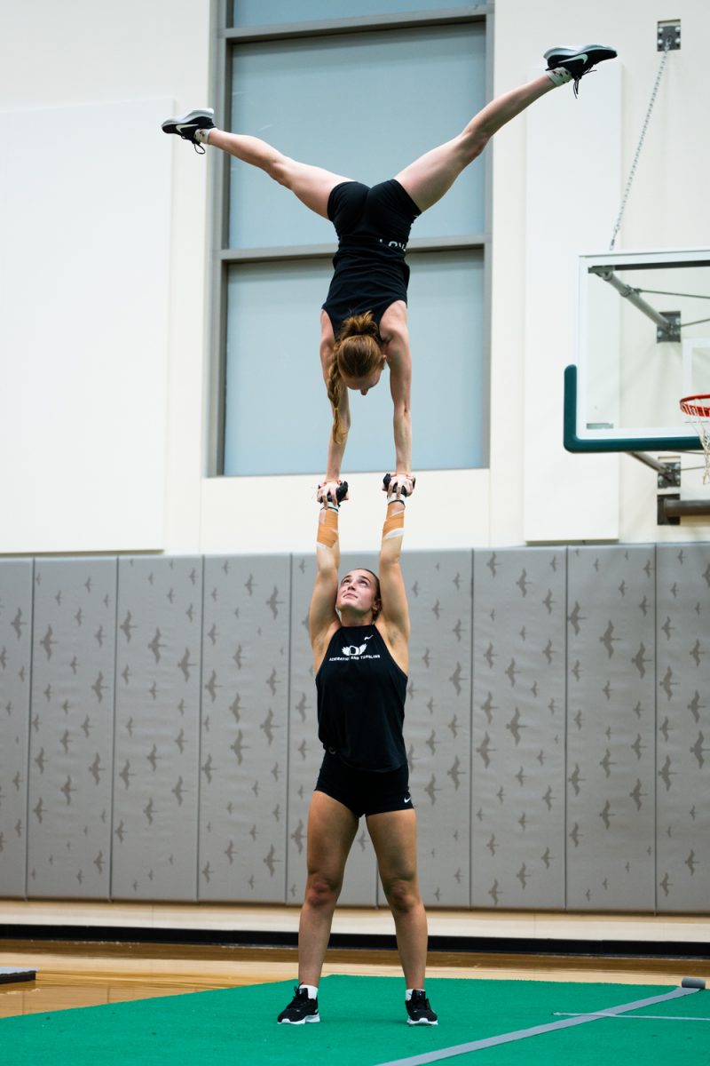 Bella Swarthout (10) mid routine, holding up Bethany Glick (5). The University of Oregon Ducks Acrobatics and Tumbling team practices at Matthew Knight Arena in Eugene, Ore., on Feb. 6, 2025. (Rowan Campbell/Emerald).