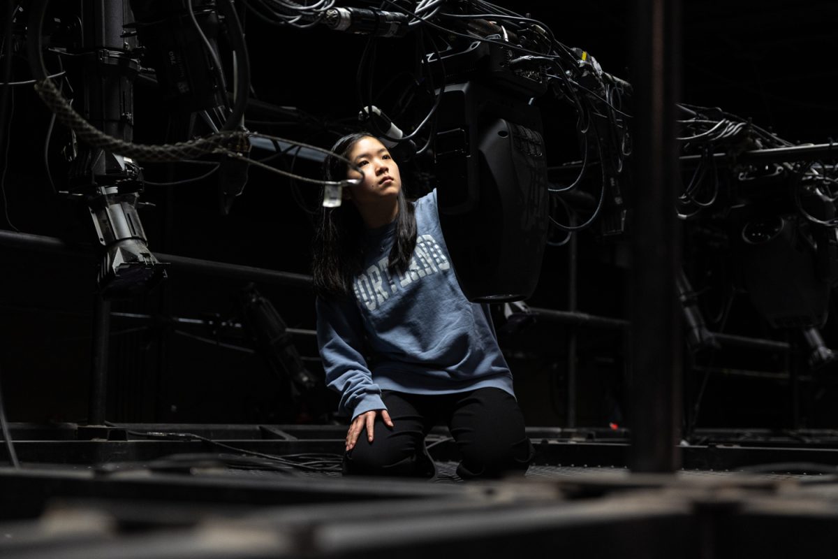 Ayano Yamada kneels above the Hope Theatre stage and adjusts a light. (Molly McPherson/Emerald)