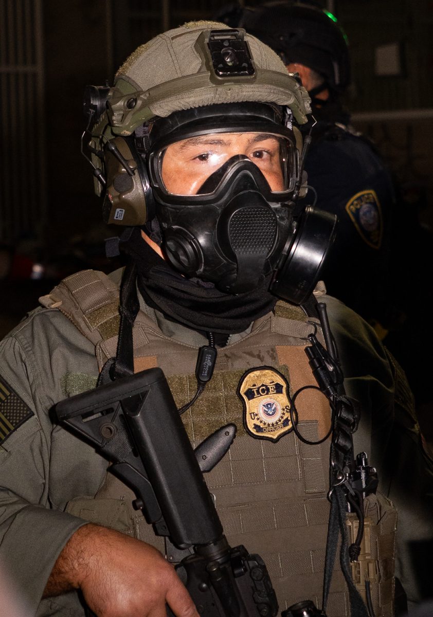 A United States Border Patrol agent holds a crowd control weapon as he pears into the crowd of demonstrators. On June 14 around 6:30 p.m. the Portland Police Bureau declared a riot at the Immigration Customs Enforcement Center in south Portland after four straight days of demonstrations. A crowd of roughly 200-300 endured multiple tear gas cans being thrown throughout the night, from roughly 6:30 p.m. until 1 a.m. Demonstrators threw rocks and plastic water bottles at the ICE facility, with several federal authorities periodically deploying pepper spray and shooting pepper spray balls to control the crowd. At the end of the night, three demonstrators had been arrested. (Saj Sundaram/Emerald)