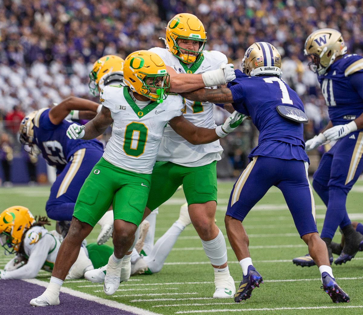 Oregon Ducks running back Jordon Davison (0) and multiple Ducks players are pushed off the field as they attempt to block for Oregon Ducks running back Noah Whittington (6). The No. 6 University of Oregon Ducks take on the University of Washington Huskies at Husky Stadium in Seattle, Wash. on Nov. 29, 2025. (Saj Sundaram/Emerald)