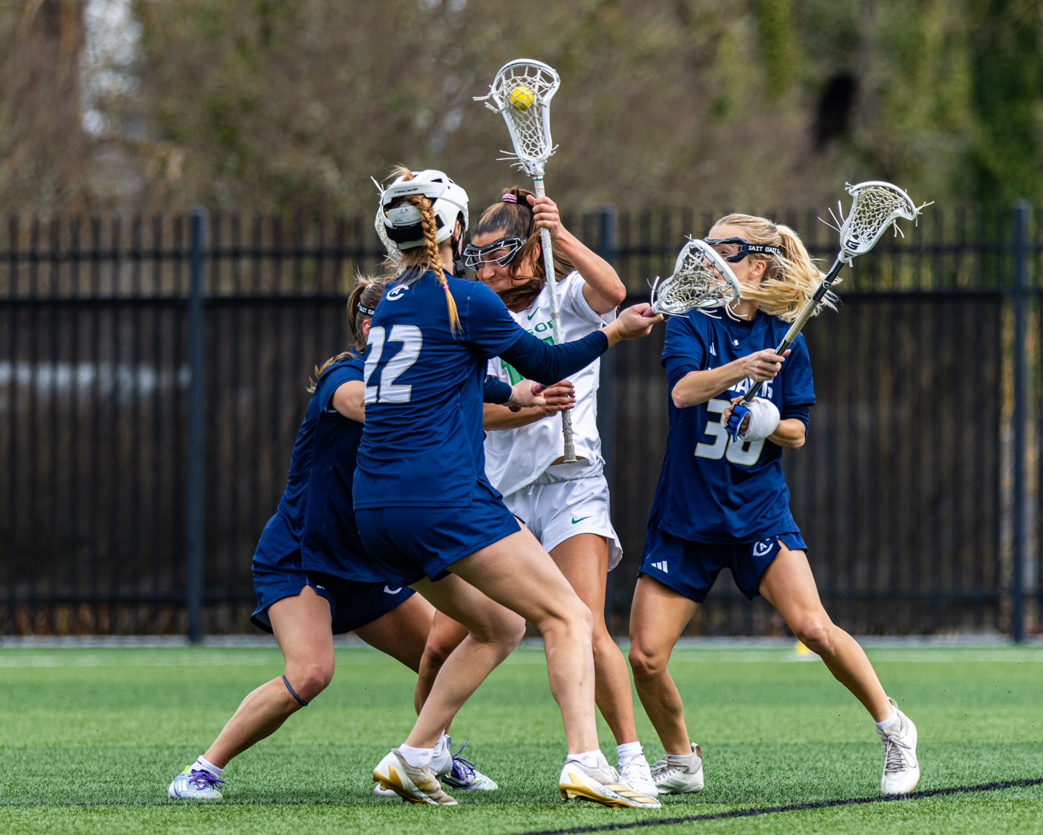 Oregon midfielder Jenae Sperling (19) holds the ball high as UC Davis players Lola Chai (24), Ava Horrocks (22), and Audrey Carr (30) converge on her. The Oregon Ducks women’s lacrosse hosted the UC Davis Aggies at Pape Field in Eugene, Ore. on Feb. 28, 2026, winning 10-9. (Owen Burriss/Emerald)