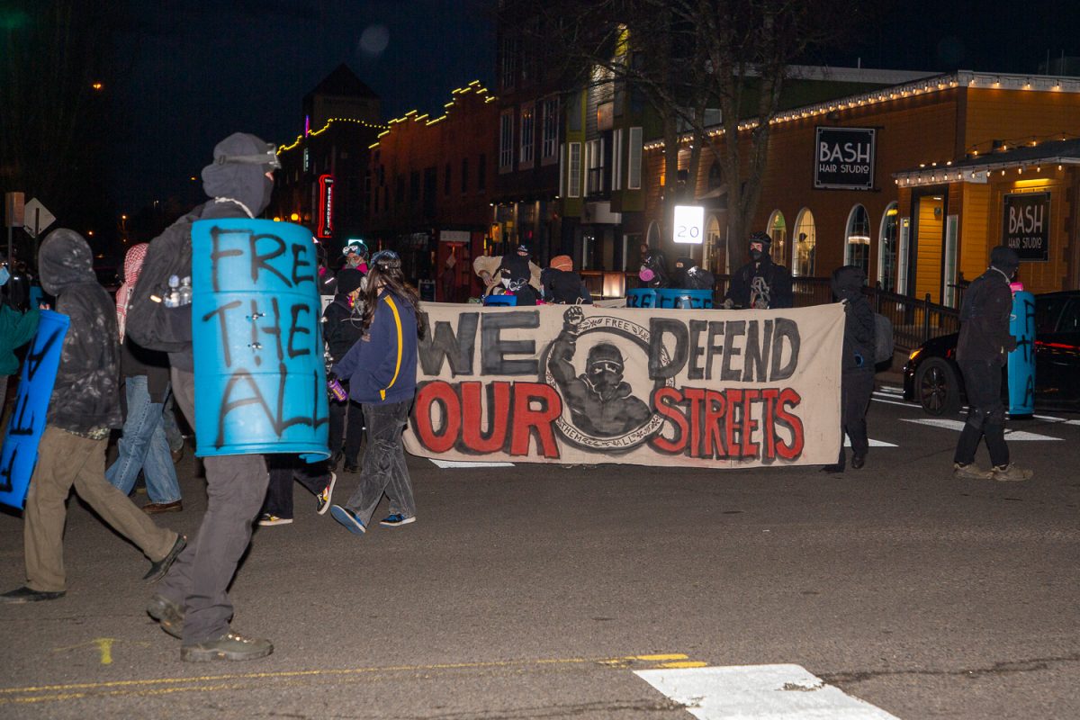 Protesters turn onto High Street holding a sign reading "We Defend Our Streets" while chanting "no business as usual" on Feb. 28, 2026. (Corey Hoffman/Emerald)