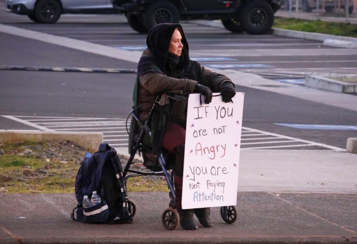 Ann Marie Brittan sits on the corner of 7th St & Pearl Ave.  with a sign that reads "If you are not Angry, you are not paying attention