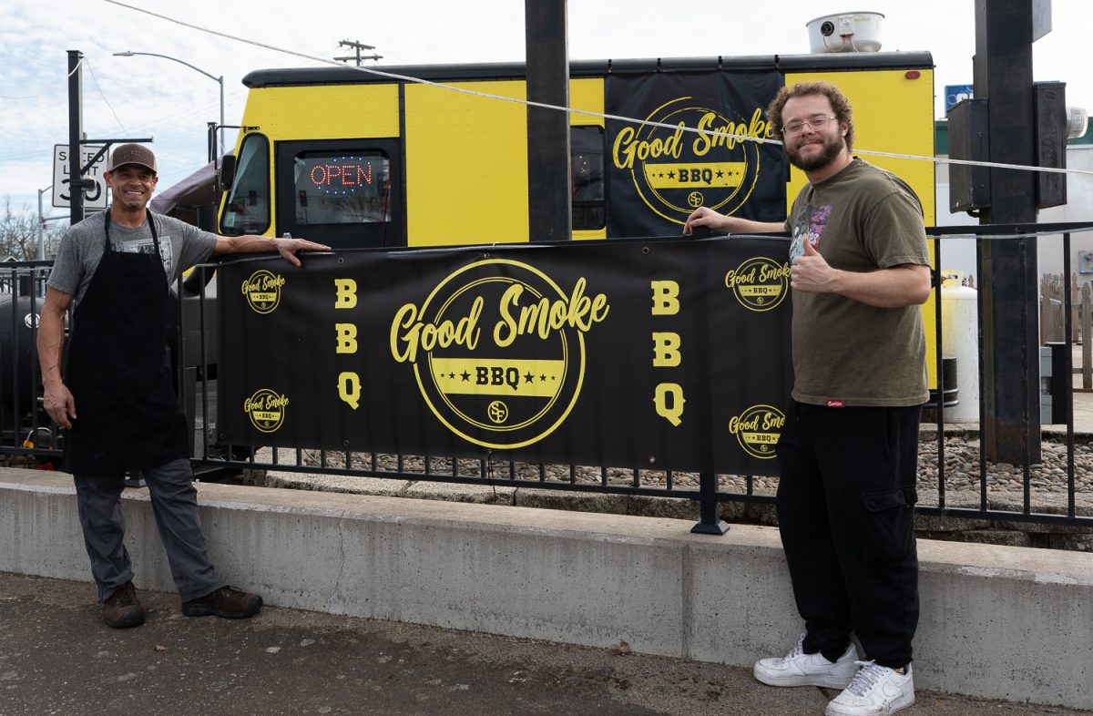 Scott Dougherty (left) and Demitrey Dougherty (right) stand with the sign outside their food truck stall. Good Smoke BBQ, a food truck on Chambers and West 7th Ave. in Eugene, Ore., on Mar. 19, 2026, offers a variety of ribs and other meals such as pulled pork sandwiches. The owner, Scott Dougherty runs the truck with his son Demitrey Dougherty, where they make and prepare every sauce, meat and bread by hand. (Saj Sundaram/Emerald)