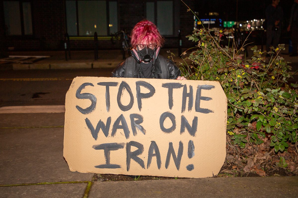 A protester sits behind a sign reading “Stop the War on Iran!” during a “No War in Iran” demonstration organized by the Party for Socialism and Liberation at the Wayne L. Morse Courthouse on March 2, 2026 in Eugene, Ore. (Corey Hoffman/Emerald)